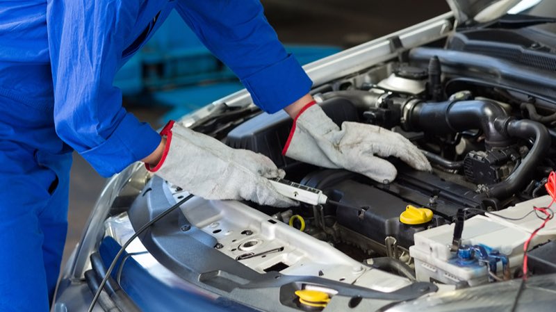 A mechanic in blue coveralls working under the hood of a vehicle